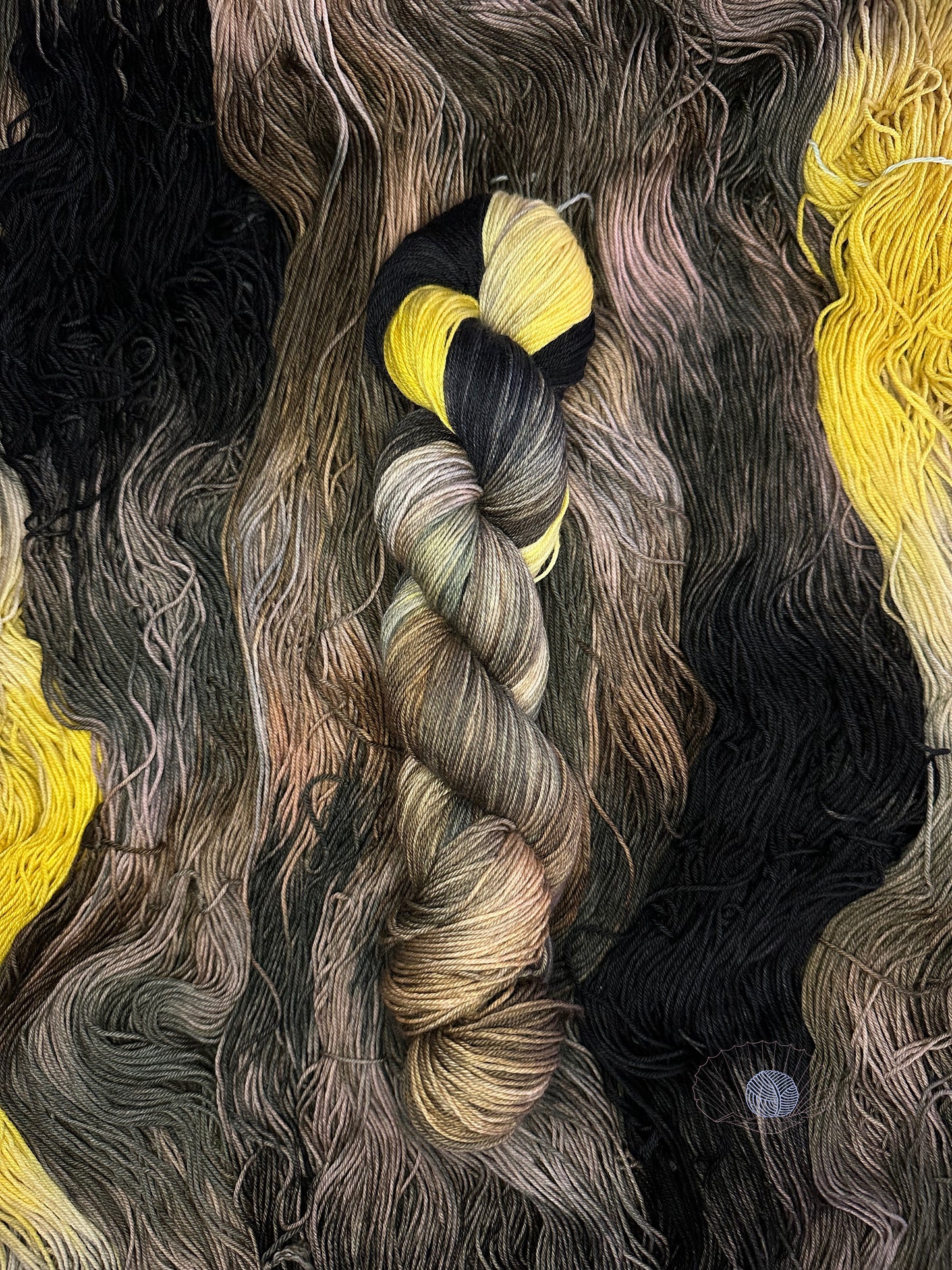 A variegated sock weight yarn with mixed shades of grey and brown sandwiched by warm yellow and black on opposite ends.