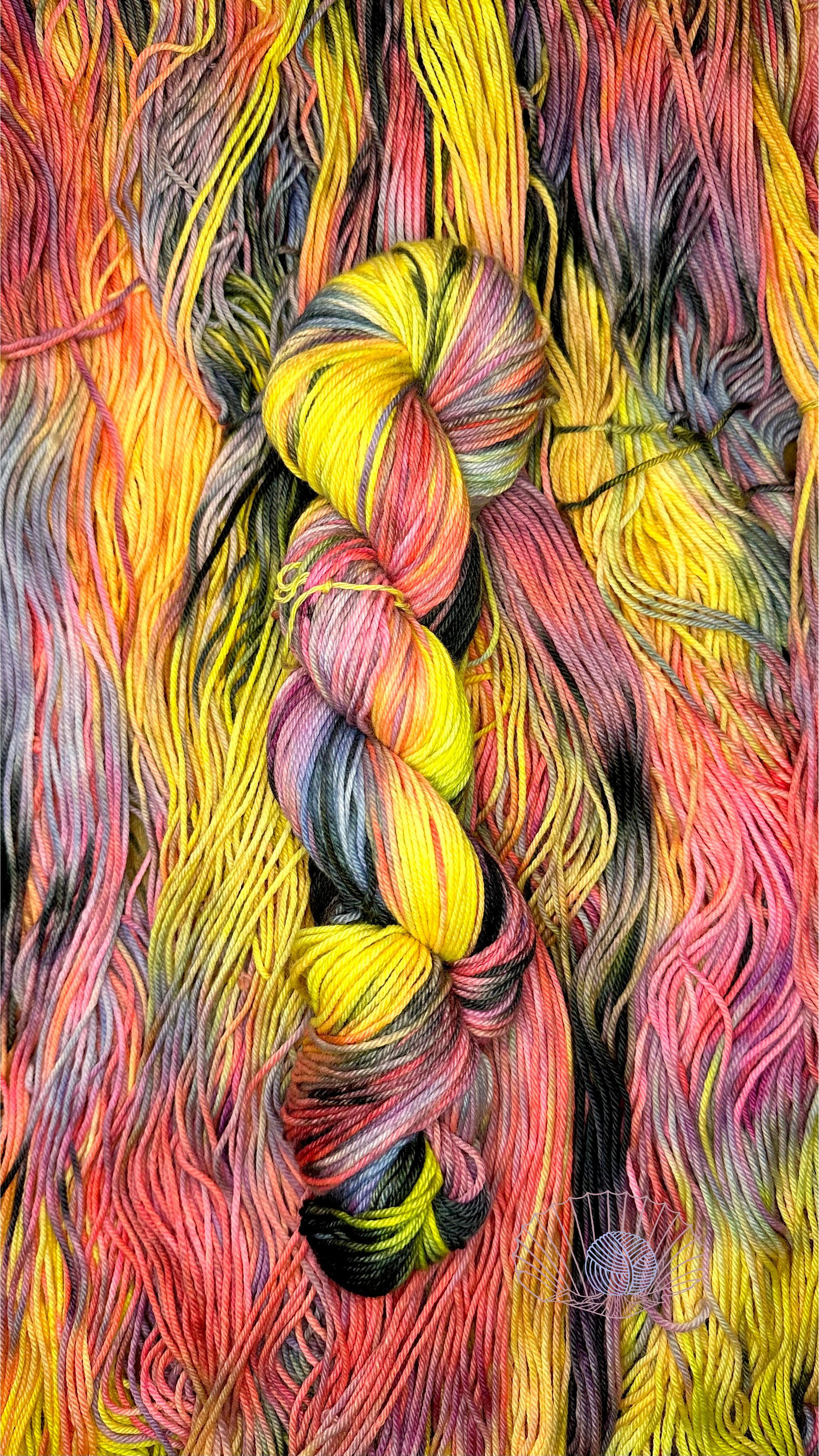 A variegated hank of yarn with yellow, pink, cool blue grey, and black laying atop untwisted hanks of the same style.