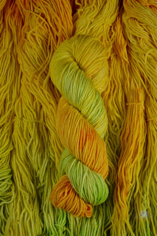 A gradient of orange to yellow to citron with speckling. Dyed on worsted weight yarn.