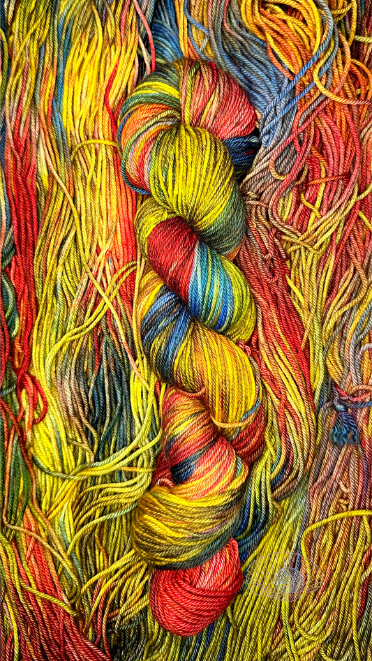 A variegated hank of yarn consisting of dusky shades of red, yellow, and blue sitting atop a pile of untwisted hanks of the same kind.