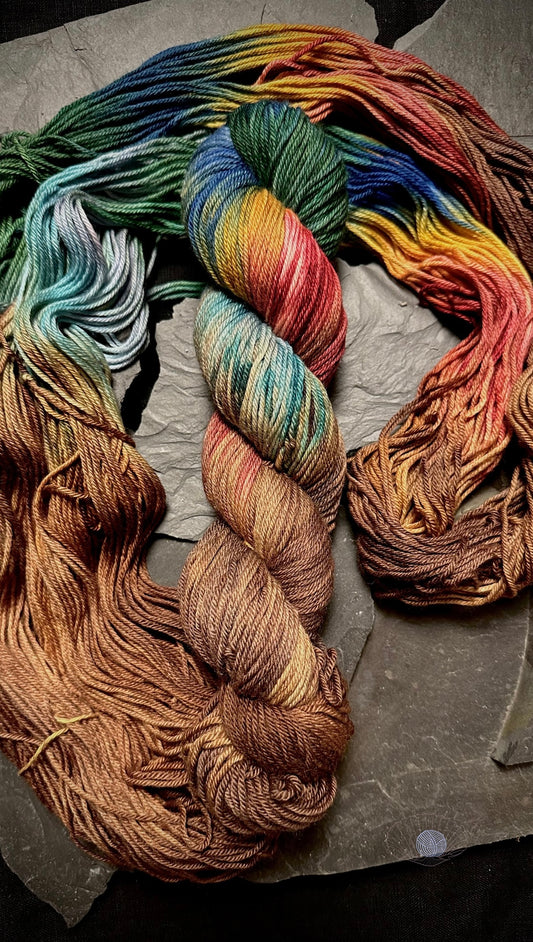 A variegated yarn with colorblock stripes of oxblood, mustard, royal blue, forest green, steel, and robin’s egg blue sandwiched by walnut wood toned ends