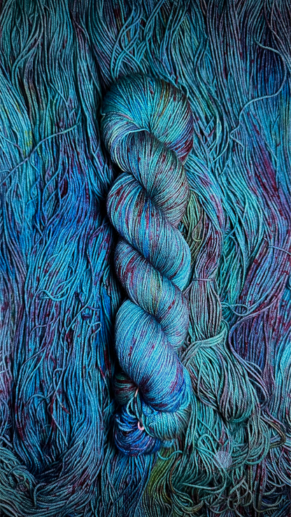 A variegated sock weight yarn with an aqua base, hints of green and royal blue with dark red speckling