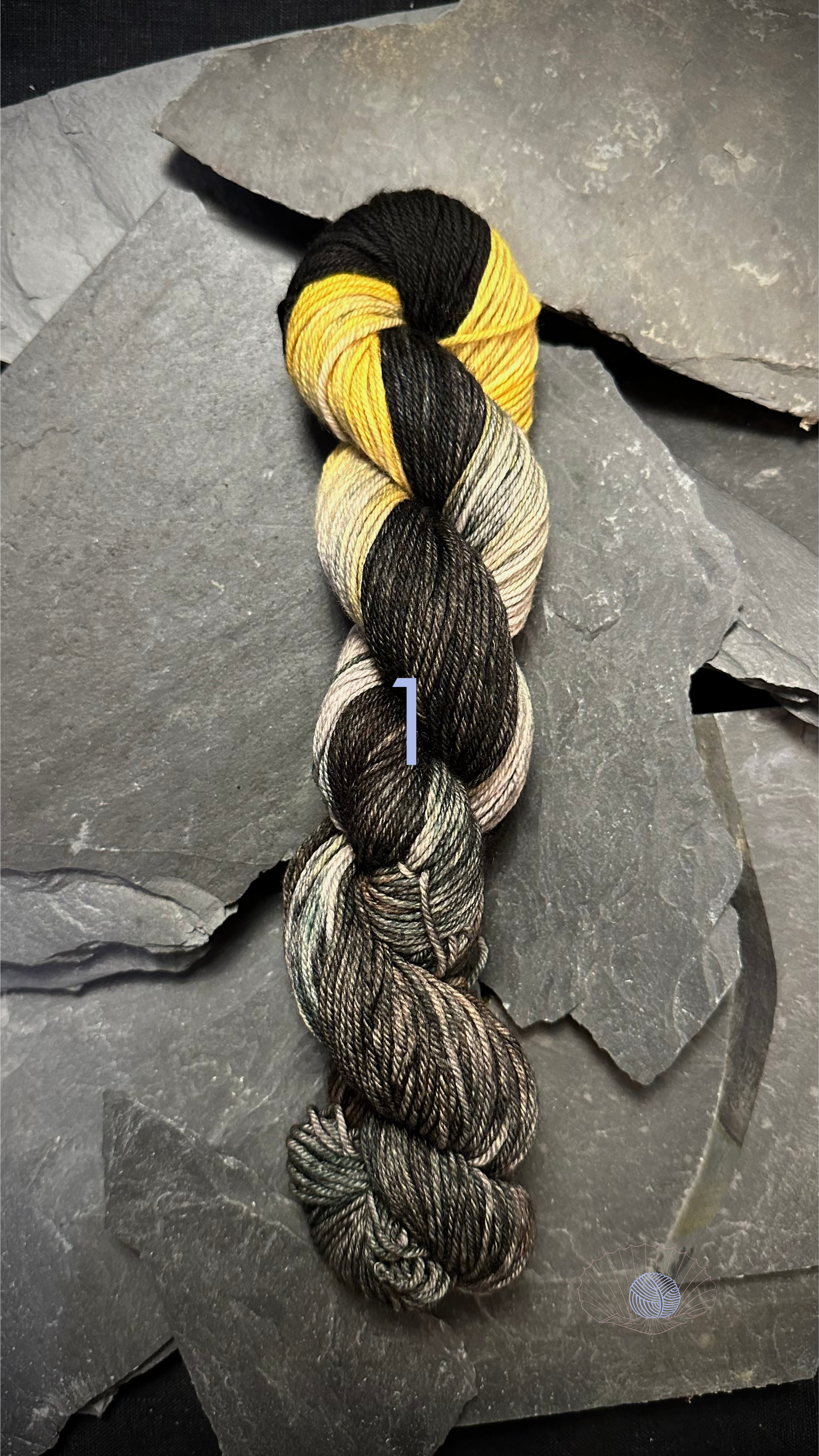 A variegated DK weight yarn with black and yellow at the top and shades of grey on the lower half