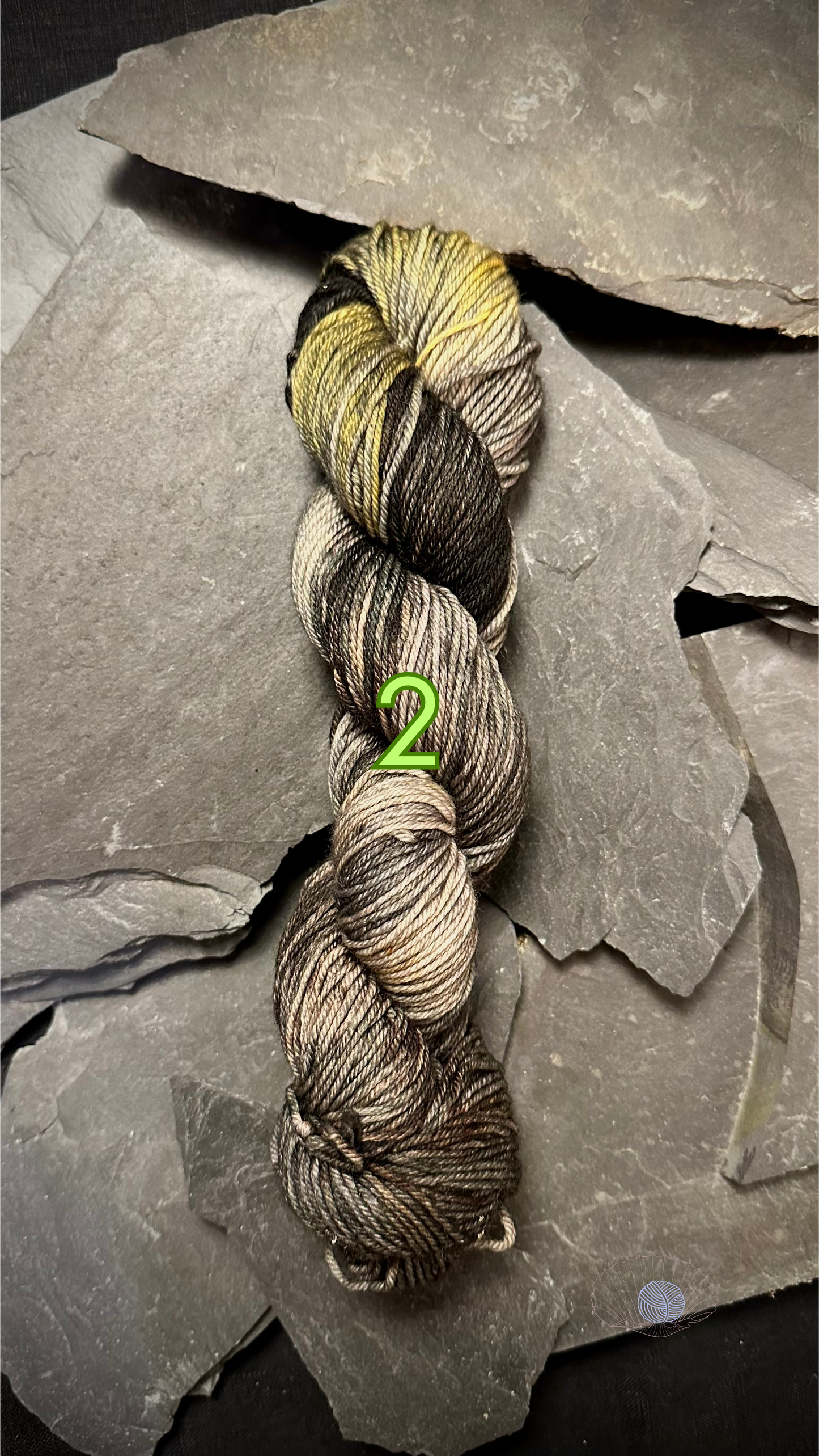 A variegated DK weight yarn with faded yellow and black at the top and light shades of grey and brown on the bottom half