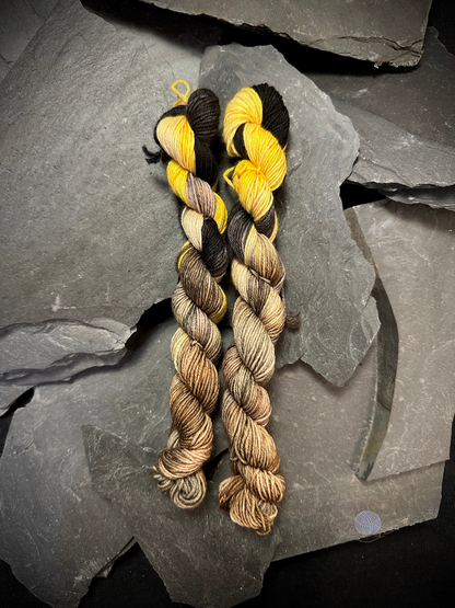 Two mini hanks of sock weight yarn with black and bright yellow at the top and shades of brown and grey on the bottom half