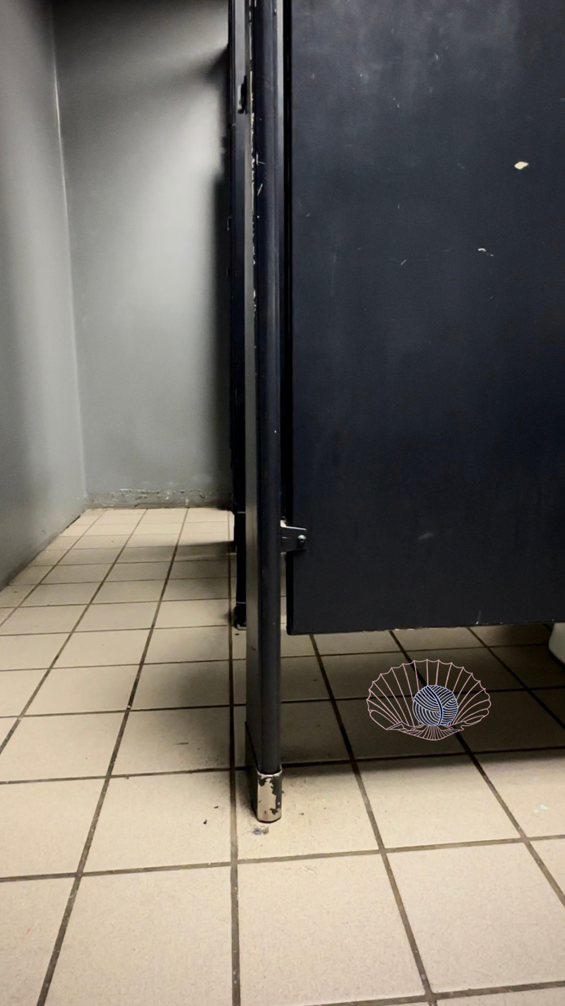 A hip level view of navy bathroom stalls with off white square tiles and grey walls.