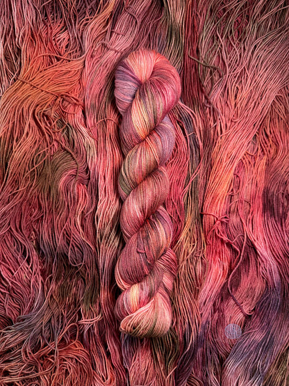 A variegated sock weight yarn with shades of pink, salmon, burgundy, purple, and brown