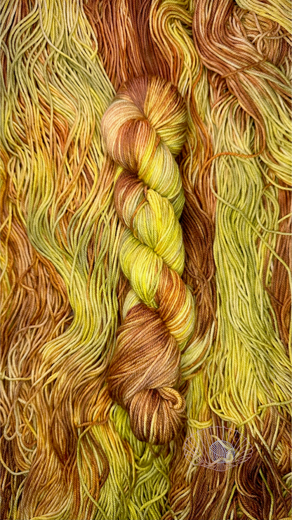 A variegated hank of yarn consisting of light acid green and light warm brown sitting atop a pile of untwisted hanks of the same kind.