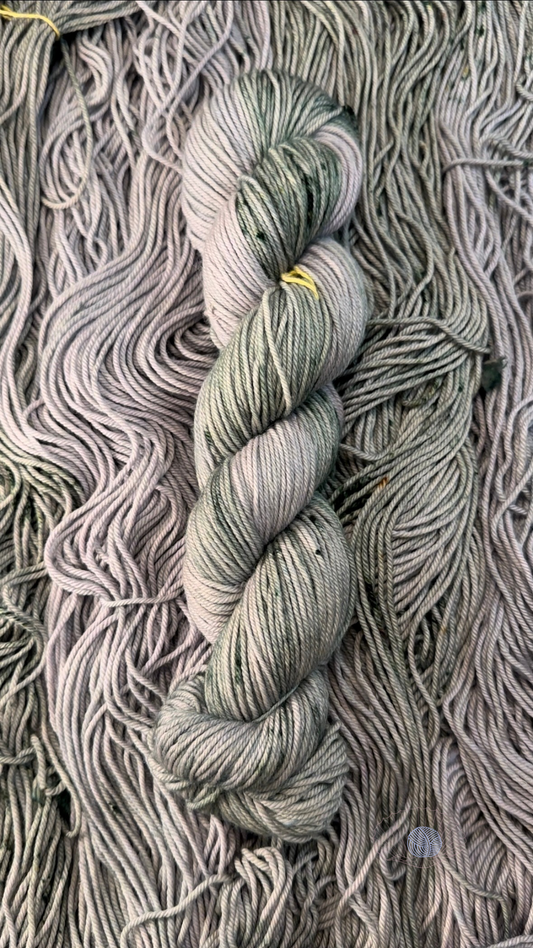 A DK weight yarn with a tonal base of soft light grey accompanied by dark green speckling